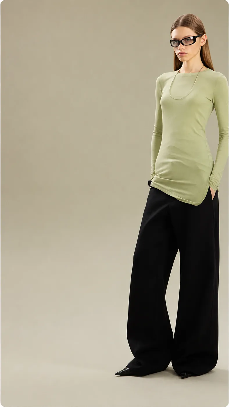Model in a sage long-sleeve top and wide black trousers